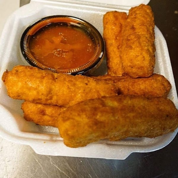 Golden-brown mozzarella sticks and a cup of marinara sauce in a white takeout container.