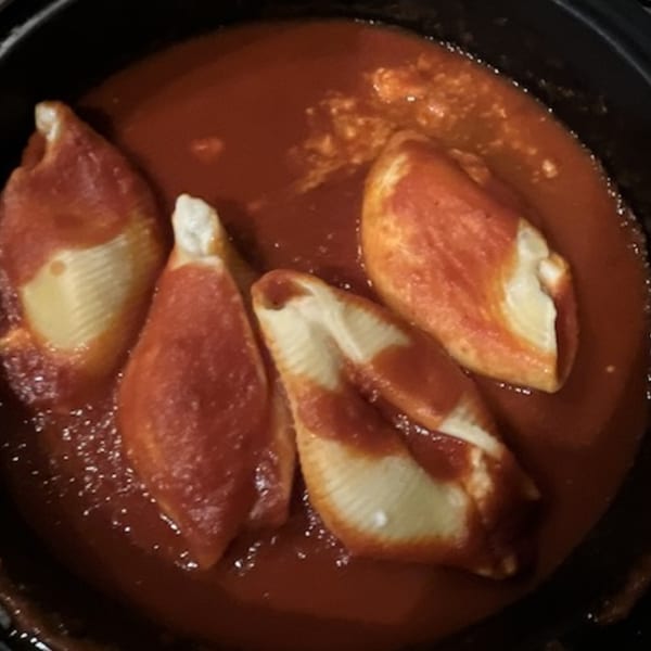 Four stuffed pasta shells covered in rich red tomato sauce in a black pan.